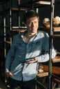 Confident young business man using digital tablet while standing near shelves in office room. Royalty Free Stock Photo