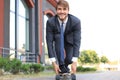 Confident young businessman in business suit on longboard hurrying to his office, on the street in the city