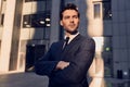 Confident young businessman keeping arms crossed and looking at camera on cityscape background Royalty Free Stock Photo