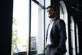 Confident young businessman looking at camera while standing near the window an office building. Royalty Free Stock Photo