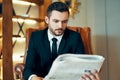 Confident young businessman reading newspaper and latest news while sitting in armchair Royalty Free Stock Photo