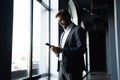 Confident young businessman using smartphone while standing near the window an office building. Royalty Free Stock Photo
