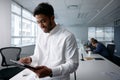 Confident young businessman in businesswear smiling and using digital tablet in office