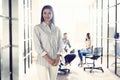 Confident young businesswoman standing with her arms crossed in a modern office with colleagues working in the Royalty Free Stock Photo