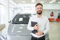 Confident young caucasian businessman shop assistant standing in car automobile dealer shop