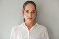 Confident young Caucasian woman in white shirt looking at camera on grey background, authentic half body portrait. Young