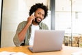 Confident young entrepreneur using laptop and talking on mobile phone in contemporary co-working space Royalty Free Stock Photo