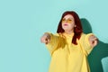 Young fatty girl with ginger hair posing a challenge pointing both index fingers at you. Waist-up portrait isolated on blue