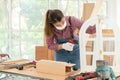 A confident young female carpenter uses a hand drill to assemble the wood window in the carpentry shop Royalty Free Stock Photo