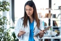 Confident young female doctor using her mobile phone while holding a clipboard and standing in the consultation