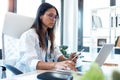 Confident young female doctor using her mobile phone while working on laptop in the consultation