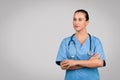 Confident young female nurse in scrubs with stethoscope around the neck, arms folded, free space