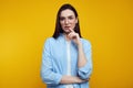 Confident young girl keeps finger near lips, looking at camera, wears eyeglasses and blue shirt, isolated over orange Royalty Free Stock Photo