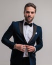 confident young groom looking forward and arranging elegant tuxedo