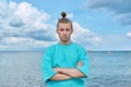 Confident young male with crossed arms looking at camera, sky sea background