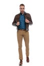 Confident young man adjusting brown leather jacket and walking Royalty Free Stock Photo