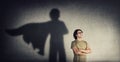 Confident young man keeps arms crossed smiling optimistic as casting a superhero with cape shadow on the wall. Motivated and Royalty Free Stock Photo