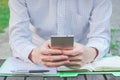 Confident young man in smart casual wear holding smart phone and looking at it while sitting at his working place in the park Royalty Free Stock Photo