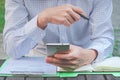 Confident young man in smart casual wear holding smart phone and pen with looking at it while sitting at his working in the park Royalty Free Stock Photo