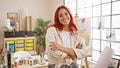 Confident young redhead artist, arms crossed, gleefully gracing the indoor art studio with her contagious smile Royalty Free Stock Photo