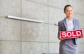 Portrait of confident young saleswoman holding sold placard while standing against wall in apartment