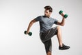 Confident young sportsman exercising with dumbbells