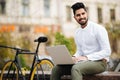 Confident young stylish indian man working on laptop computer while sitting outdoors with bicycle Royalty Free Stock Photo