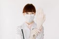 Confident young woman doctor or nurse in white coat and with medical mask posing to camera and showing how to protect