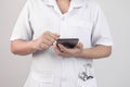 Confident young woman doctor using smartphone with stethoscope in her pocket and stand over grey background Royalty Free Stock Photo