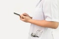 Confident young woman doctor using smartphone with stethoscope in her pocket and stand over white background. Royalty Free Stock Photo