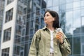 Confident Young Woman Using Earphones and Holding Cocktail in Hand While Walking in the City, Portrait of Brunette Girl Royalty Free Stock Photo