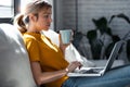 Confident young woman working with her laptop while drinking a cup of coffee sitting on a couch at home Royalty Free Stock Photo