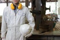 Confident young worker with safety uniform standing in factory with vertical band saws machine background. Royalty Free Stock Photo