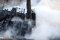 Conflagration. ruins and remains of a burnt wooden house. Burnt charred firewood in thick smoke. Royalty Free Stock Photo