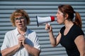 The conflict of generations. An angry middle-aged woman yells at an elderly mother through a megaphone. An adult
