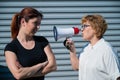 The conflict of generations. An old woman yells into a megaphone at her middle-aged daughter against gray background