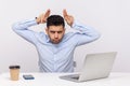 Conflict at work. Aggressive man employee sitting office workplace and showing bull horn gesture, threatening Royalty Free Stock Photo