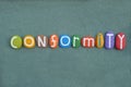 Conformity, creative word composed with multi colored stone letters over green sand