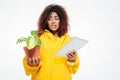 Confused african woman in raincoat holding plant Royalty Free Stock Photo