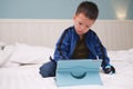 Confused aggressive Asian toddler boy child sitting in bed watching a video , playing game from tablet pc, Gadget-addicted Royalty Free Stock Photo