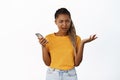 Confused and annoyed Black girl reacts to smartphone notification or phone message, shrugging puzzled and frowning