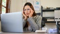 Confused Asian businesswoman looking at laptop screen, figuring out a plan to fix her problems