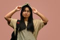 Confused asian schoolgirl putting book on her head, standing against pink background