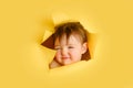 A confused baby in a hole on a paper yellow background. Torn child's h Royalty Free Stock Photo