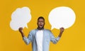 Confused black guy holding two speech bubbles on yellow background
