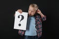Confused boy holding sheet of paper with question mark on background Royalty Free Stock Photo
