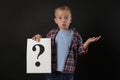 Confused boy holding sheet of paper with question mark on black background Royalty Free Stock Photo