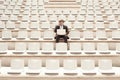 Confused Businessman Working On Laptop In Center Of Empty Auditorium