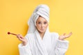 Portrait of beautiful female holding make-up brush over yellow background