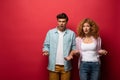 Confused couple gesturing in casual clothes isolated on red